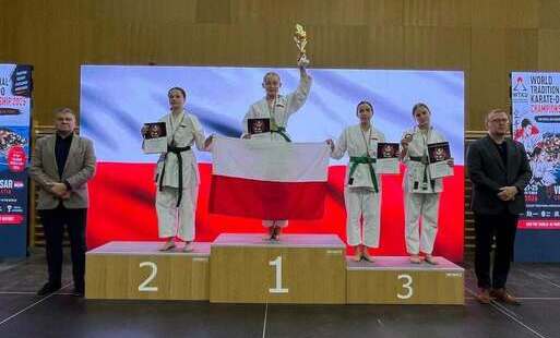 podium z zawodnikami w strojach karate, trzymającymi biało-czerwoną flagę przed sobą i puchary podniesione do góry